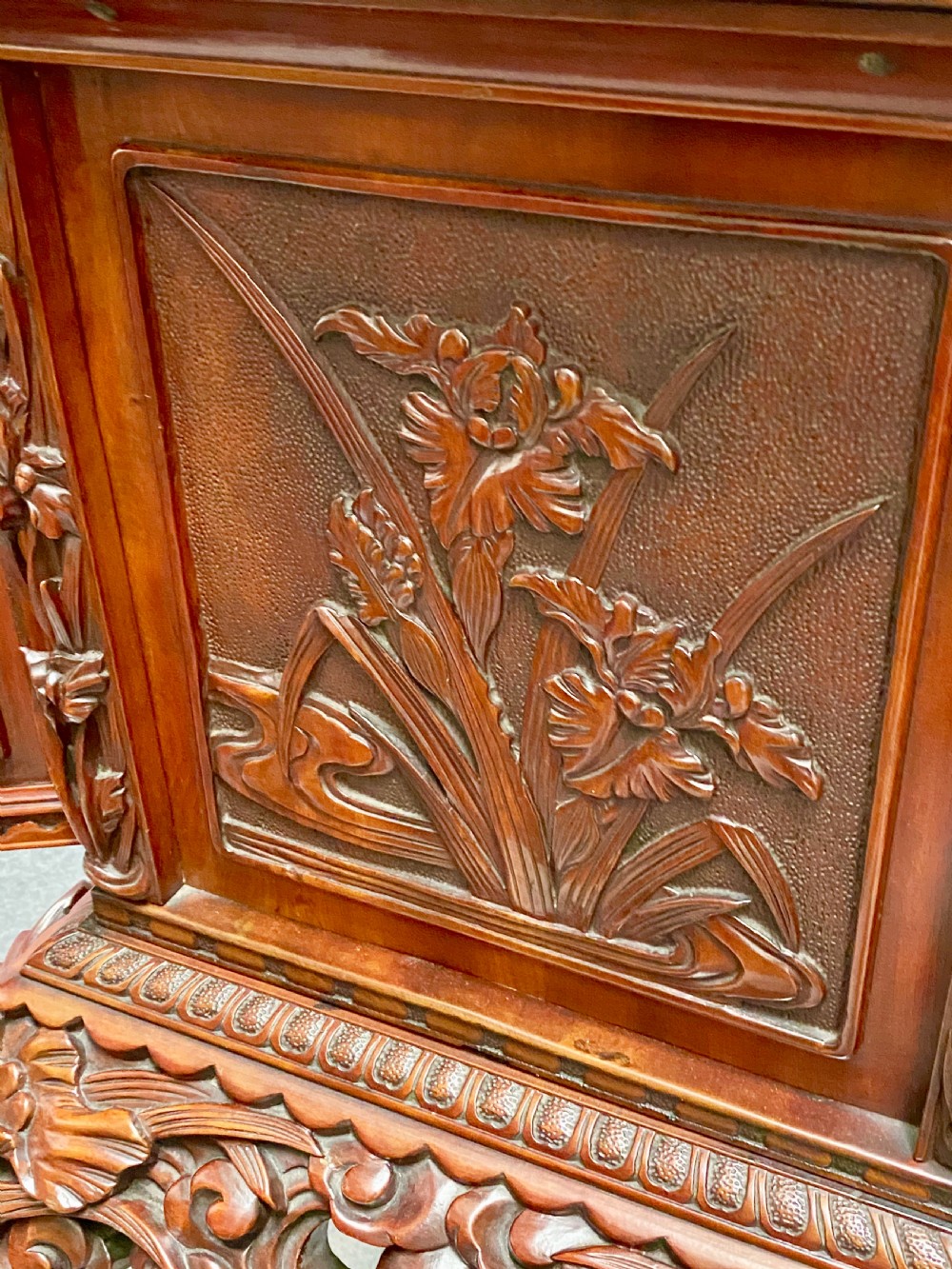 A reddish brown carved cinnabar lacquer cabinet with floral relief panels resting on a tall cabriole leg stand with an open side door. View IX