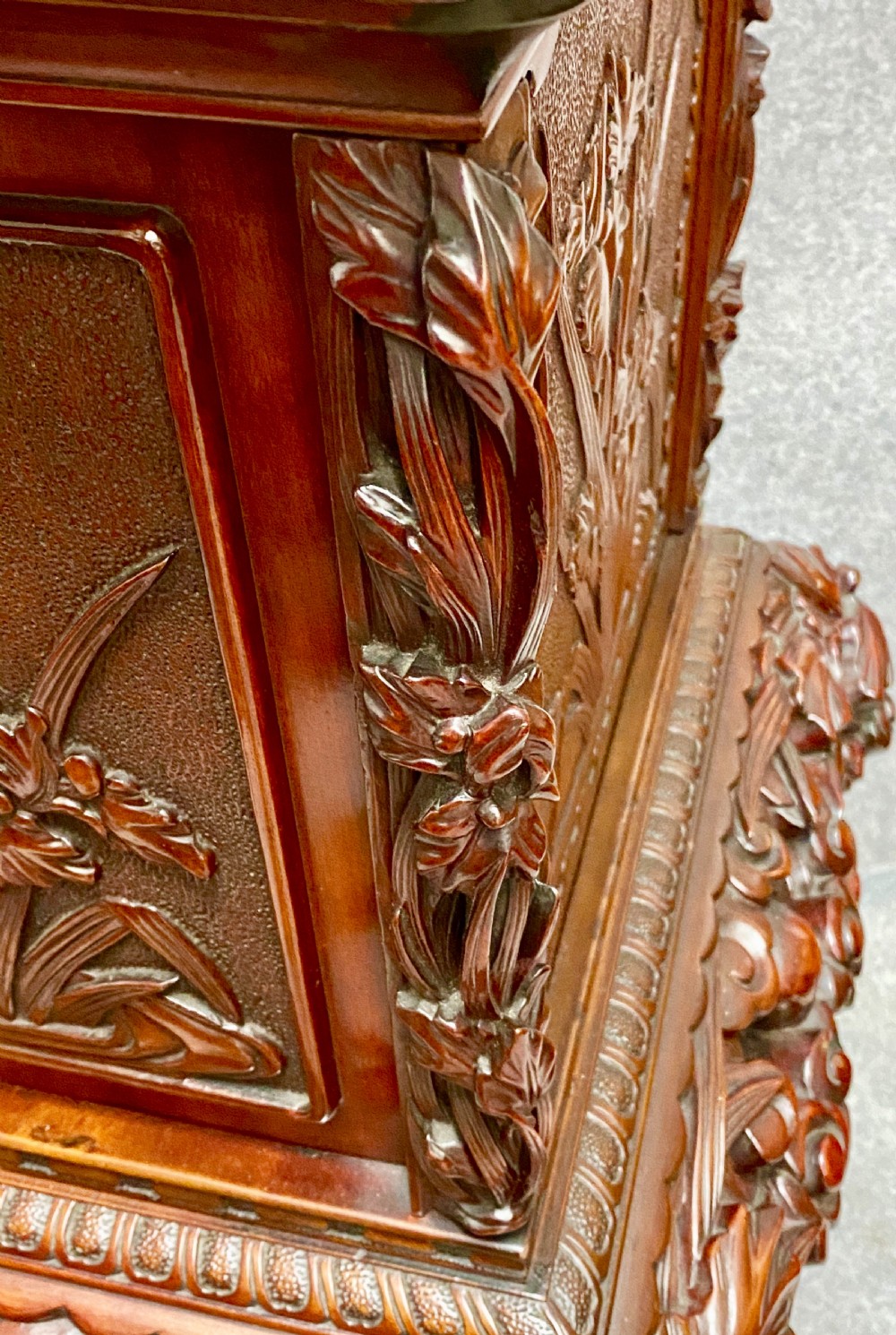 A reddish brown carved cinnabar lacquer cabinet with floral relief panels resting on a tall cabriole leg stand with an open side door. View XII