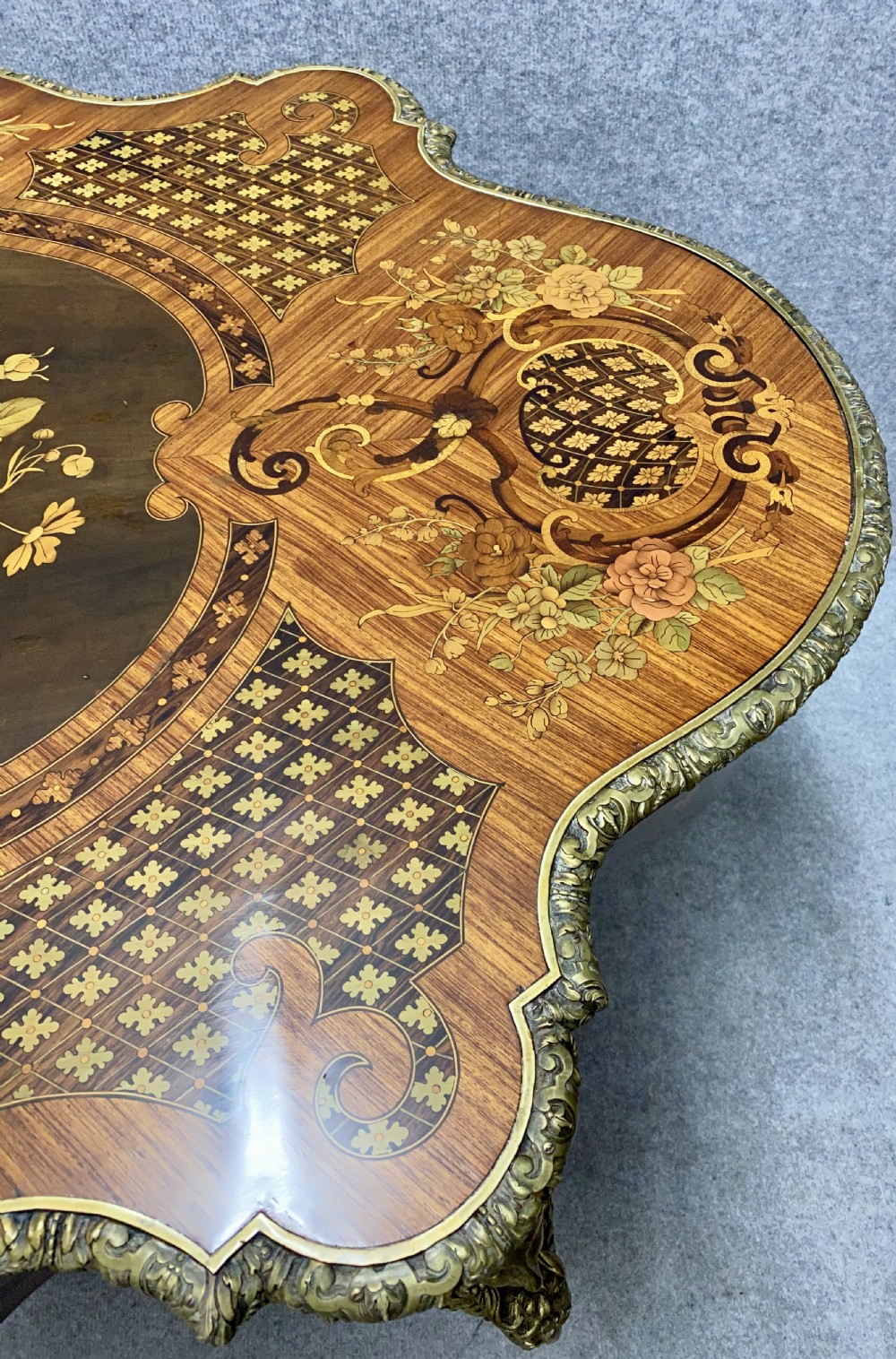 A French Louis XV style centre table featuring intricate floral marquetry inlay, a serpentine contoured top, cabriole legs, and bronze espagnolette mounts. View IV