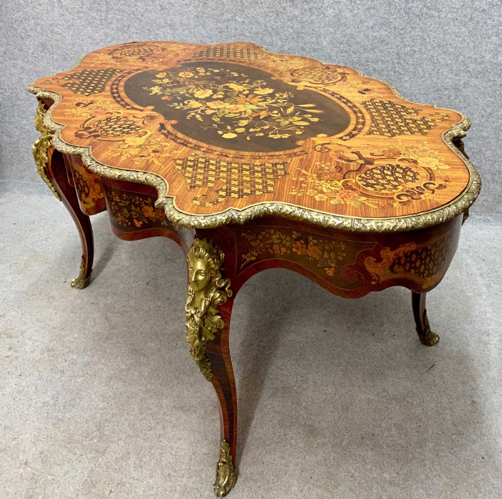 A French Louis XV style centre table featuring intricate floral marquetry inlay, a serpentine contoured top, cabriole legs, and bronze espagnolette mounts.