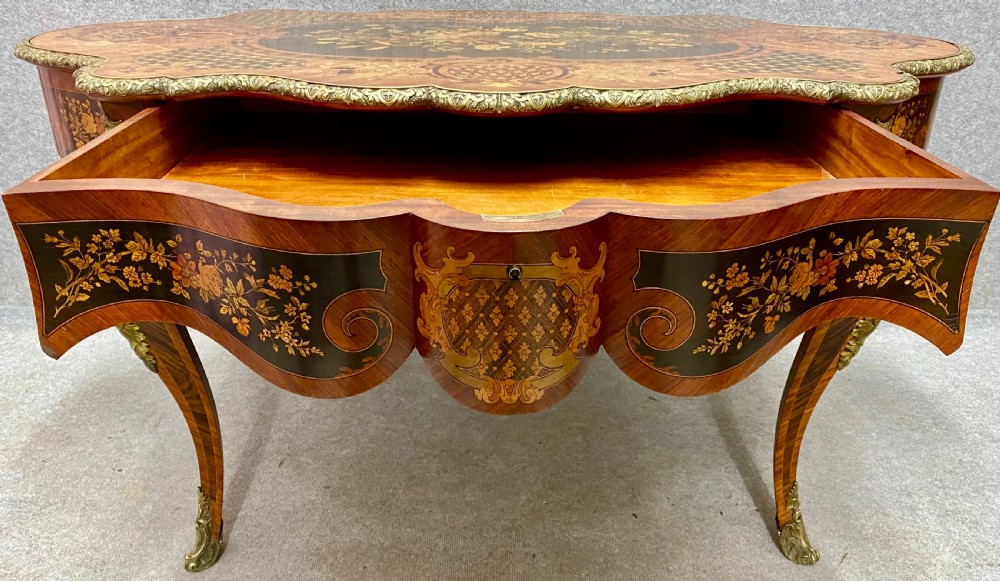A French Louis XV style centre table featuring intricate floral marquetry inlay, a serpentine contoured top, cabriole legs, and bronze espagnolette mounts. View XVI
