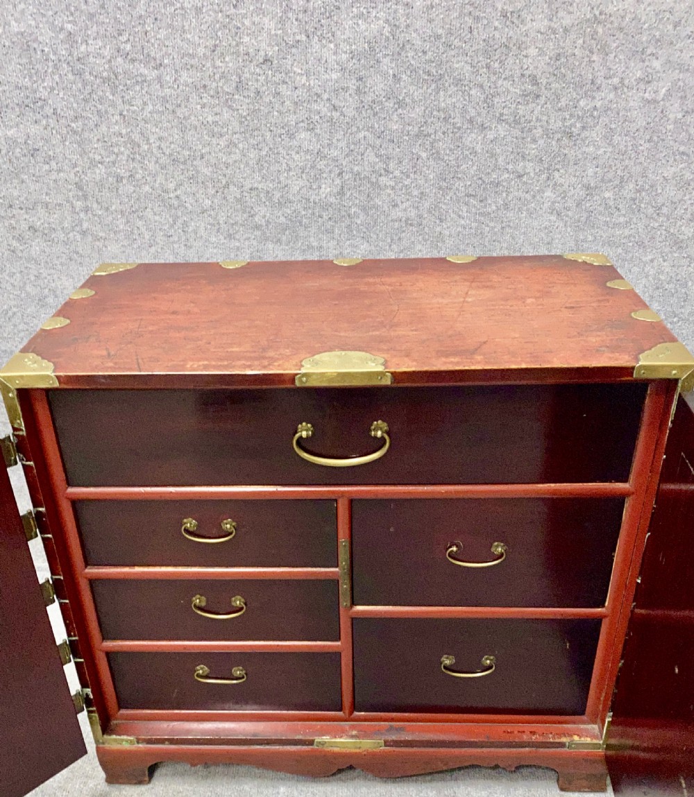 A small Chinese hardwood cabinet featuring polished dark wood, twin front doors, and decorative engraved brass mounts, hinges, and a central circular lockplate. View II