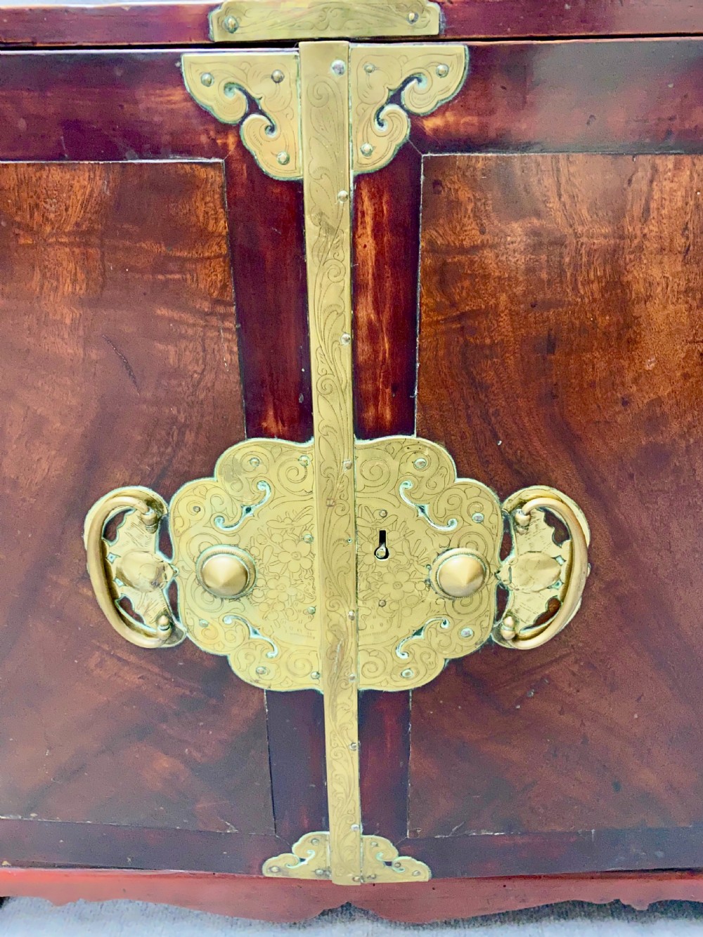 A small Chinese hardwood cabinet featuring polished dark wood, twin front doors, and decorative engraved brass mounts, hinges, and a central circular lockplate. View III