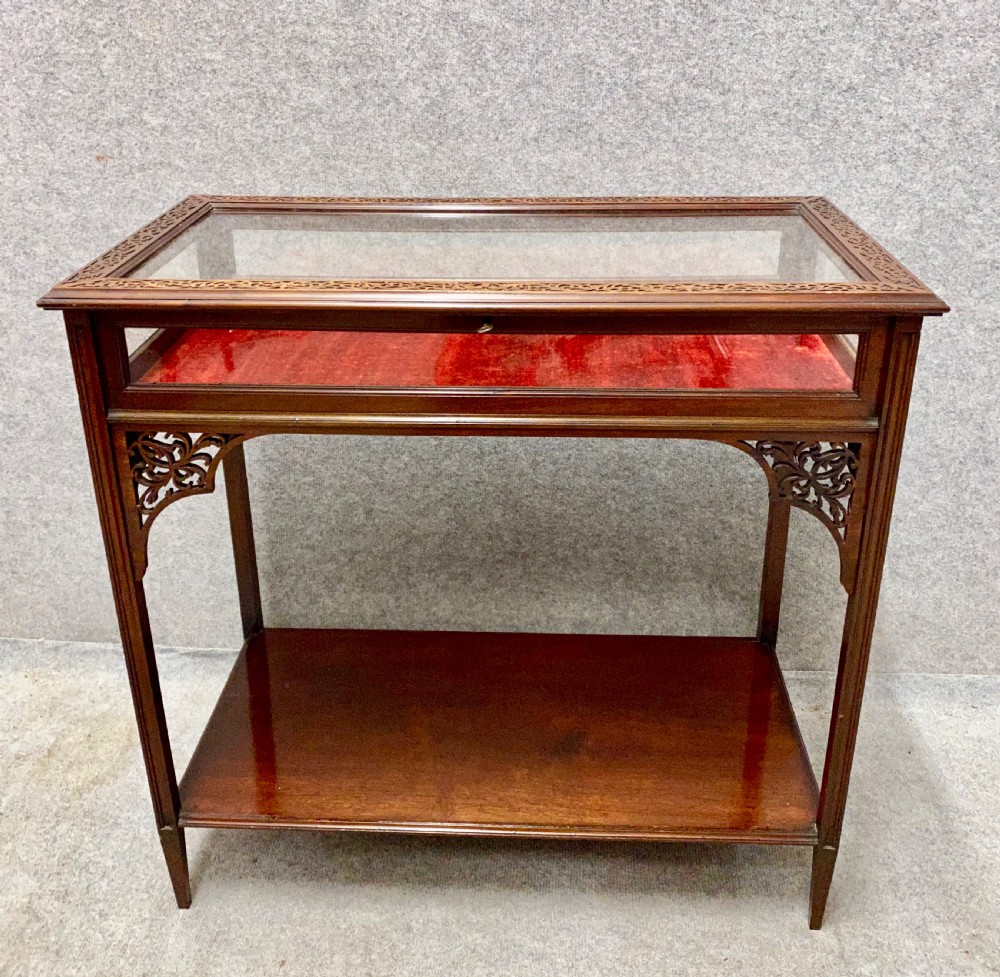 An antique glazed mahogany bijouterie table with a red fabric-lined display cavity, pierced fretwork corner brackets, and a lower shelf.