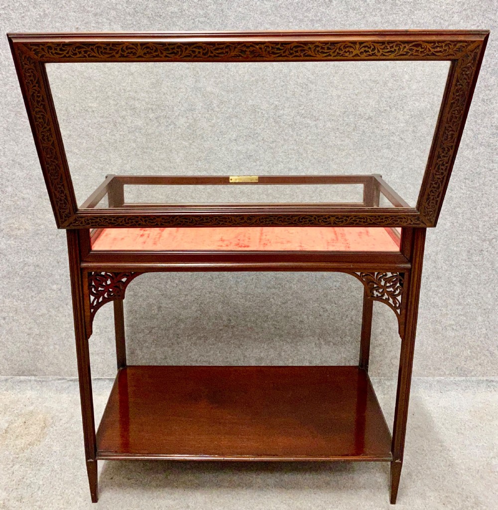 An antique glazed mahogany bijouterie table with a red fabric-lined display cavity, pierced fretwork corner brackets, and a lower shelf. View IV