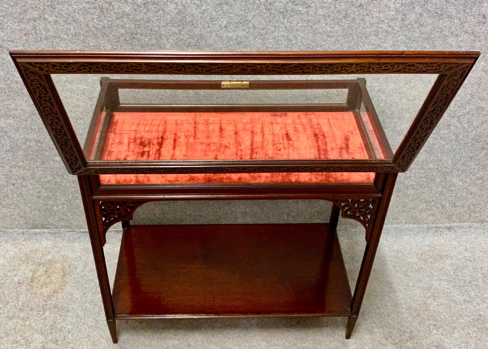 An antique glazed mahogany bijouterie table with a red fabric-lined display cavity, pierced fretwork corner brackets, and a lower shelf. View V