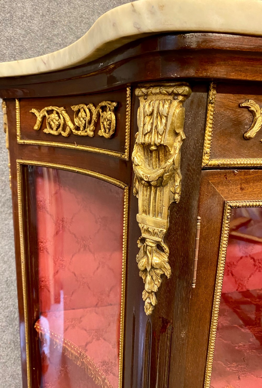 A French Louis XV style glazed display cabinet featuring serpentine glass side panels, a marble top, gilt bronze ormolu mounts, and hand-painted Vernis Martin panels at the base. View VI