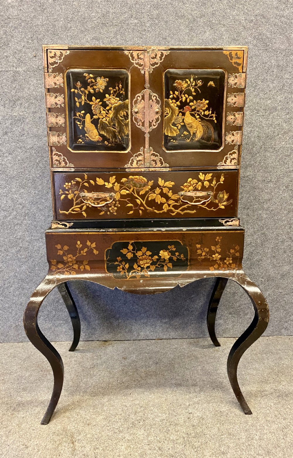 An antique Japanese Meiji period dark lacquer cabinet on a stand, decorated with gold floral and bird motifs and engraved metal mounts.