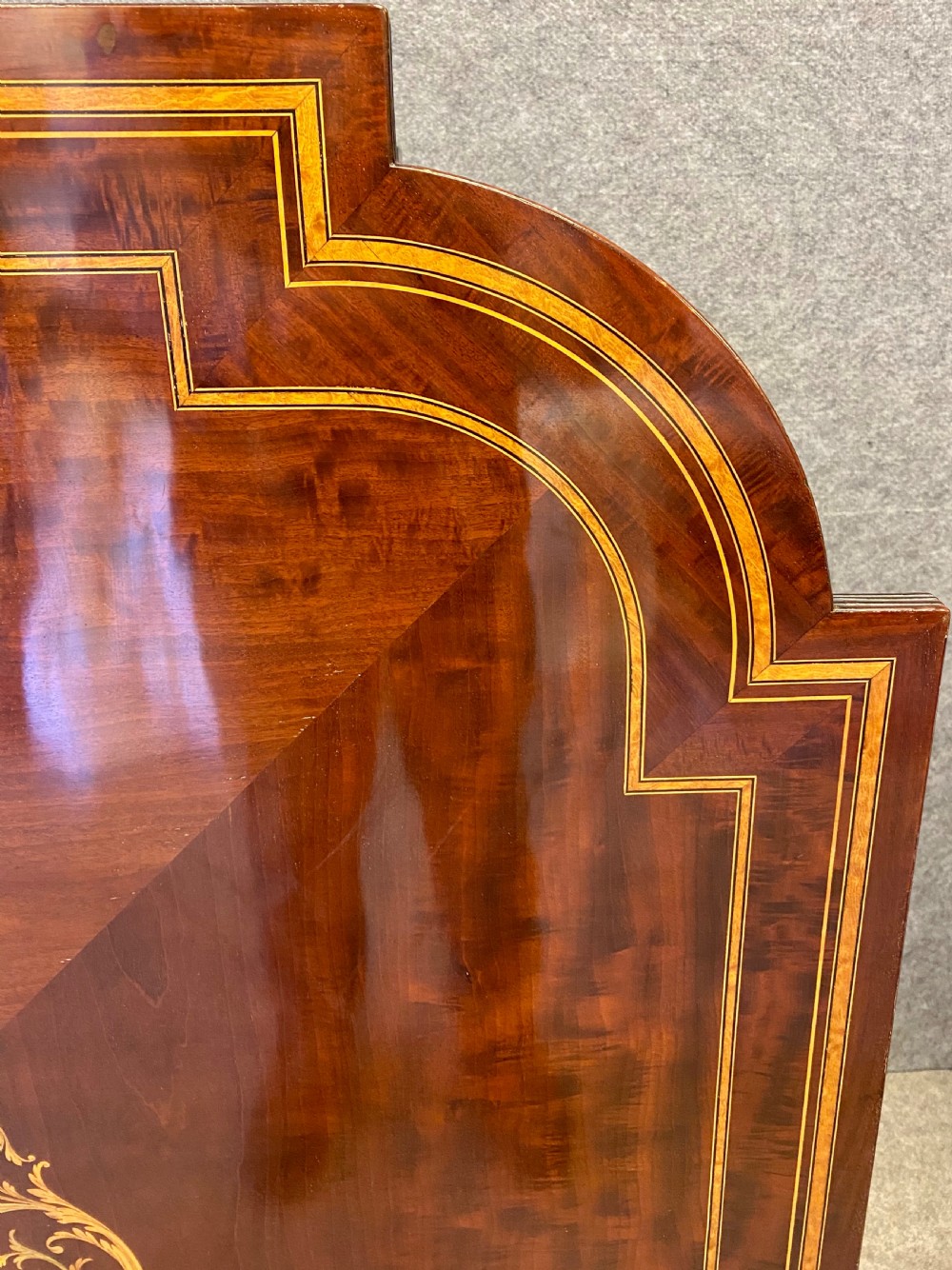 A square mahogany centre table featuring a central marquetry motif, indented corners, tapered legs, undertier, and brass castors. View IV