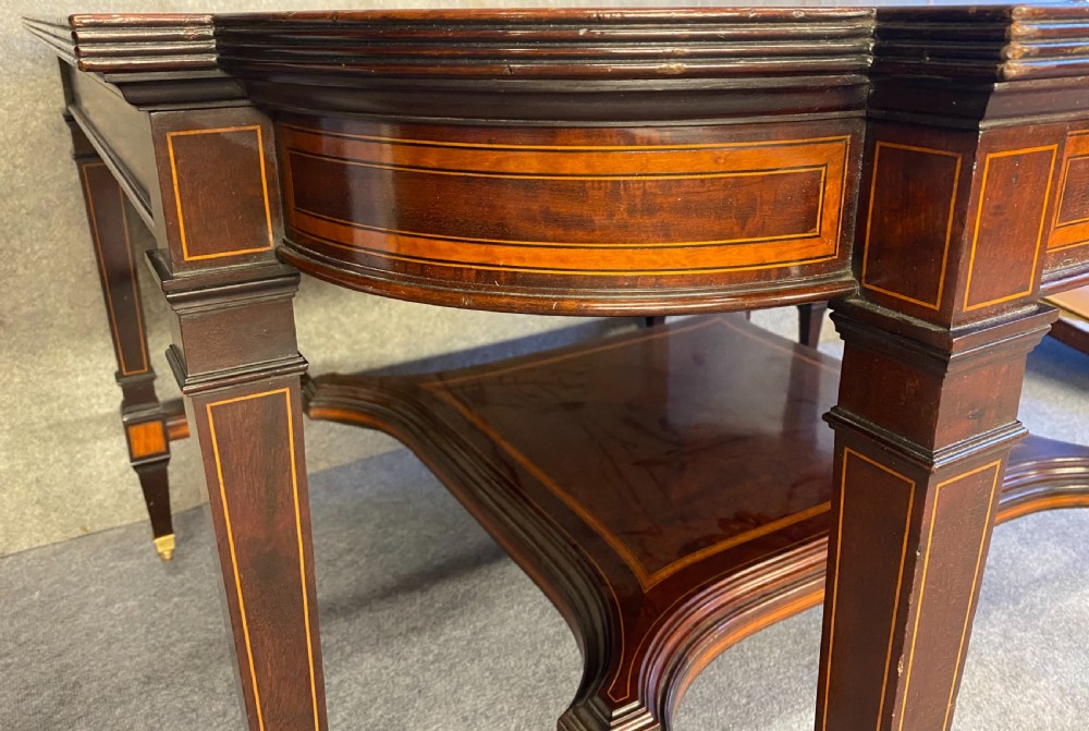 A square mahogany centre table featuring a central marquetry motif, indented corners, tapered legs, undertier, and brass castors. View V
