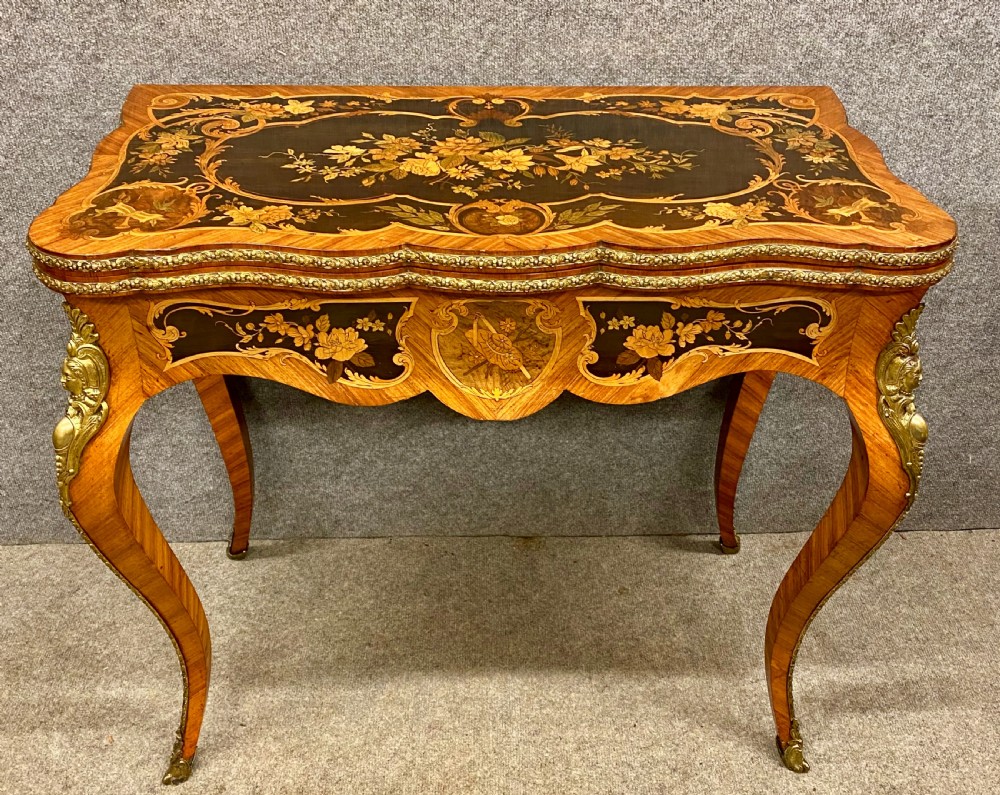 A Louis XV style serpentine card table featuring floral marquetry inlay, kingwood veneer, cabriole legs, and ornate gilt-bronze mounts.