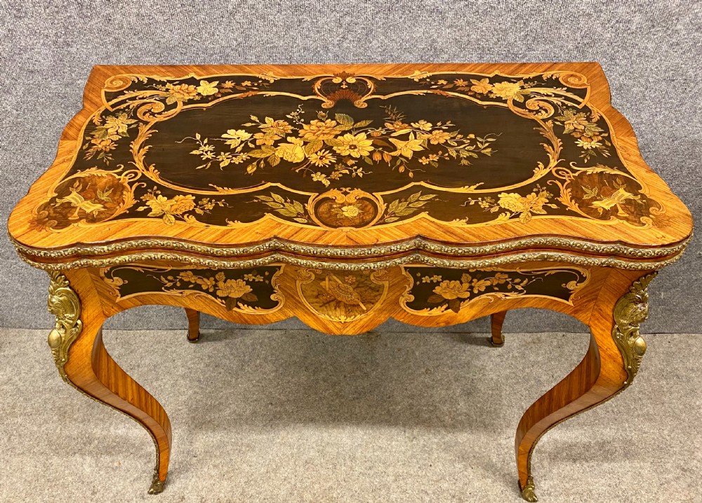 A Louis XV style serpentine card table featuring floral marquetry inlay, kingwood veneer, cabriole legs, and ornate gilt-bronze mounts. View II