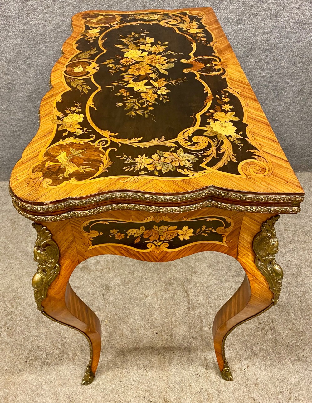 A Louis XV style serpentine card table featuring floral marquetry inlay, kingwood veneer, cabriole legs, and ornate gilt-bronze mounts. View IX
