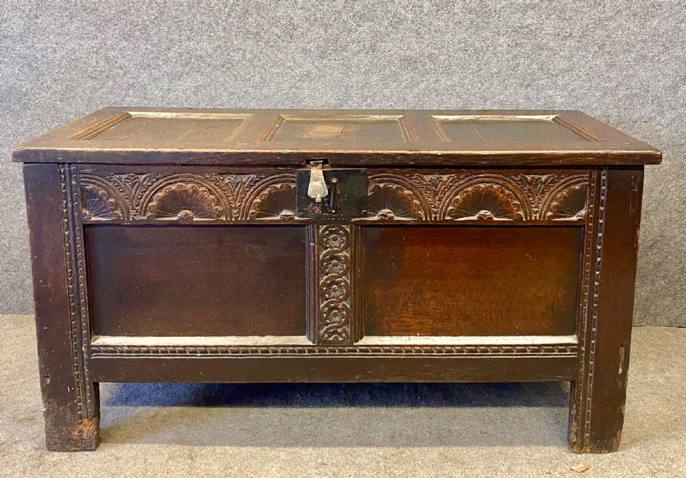 A small seventeenth-century style dark oak coffer featuring a carved lunette frieze, central rosette muntin, and an iron lock plate.