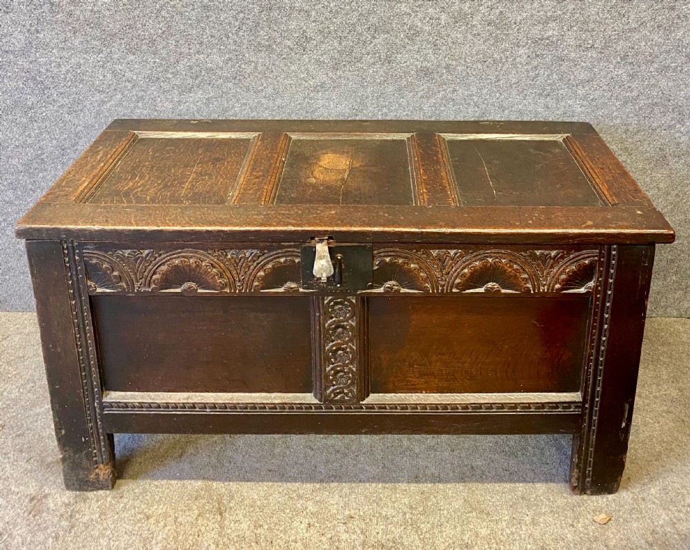 A small seventeenth-century style dark oak coffer featuring a carved lunette frieze, central rosette muntin, and an iron lock plate. View V