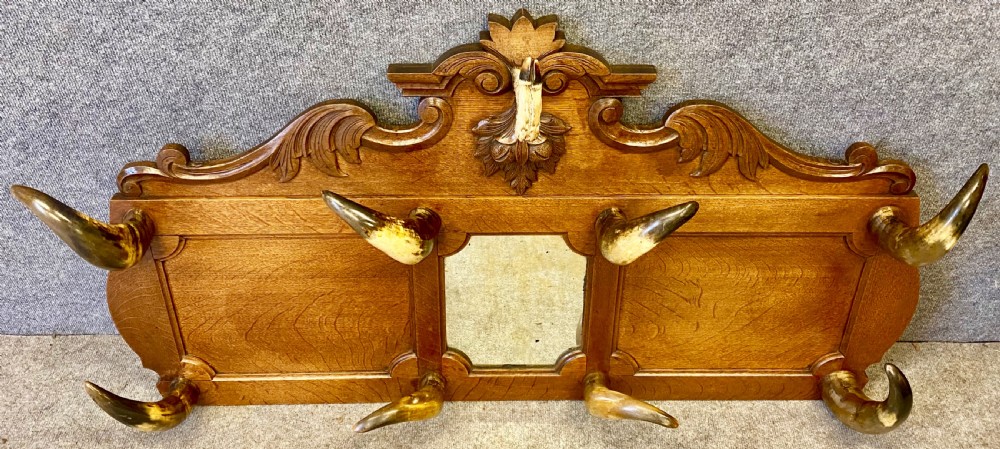 A nineteenth-century wall-mounted carved oak hall stand featuring eight horn hooks, a small central mirror, and scrollwork carving.