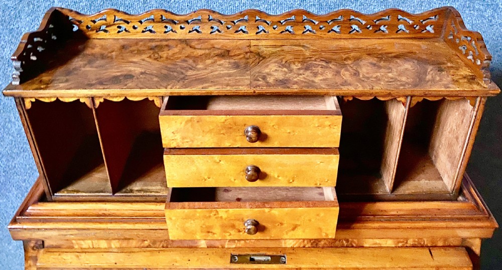 A Victorian burr walnut Davenport desk featuring an elevated pop-up stationery gallery, sloping writing slope with green leather inset, and carved front scroll legs. View VI