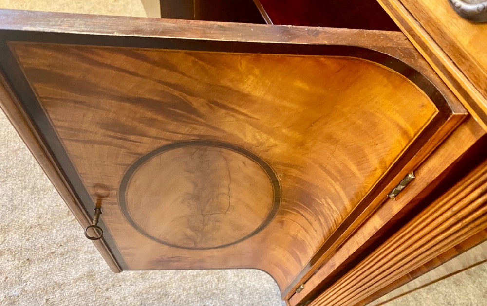 A George III satinwood cylinder desk featuring an arched cresting, a tambour roll top, two frieze drawers, and lower cupboard doors with oval inlay panels. View VII