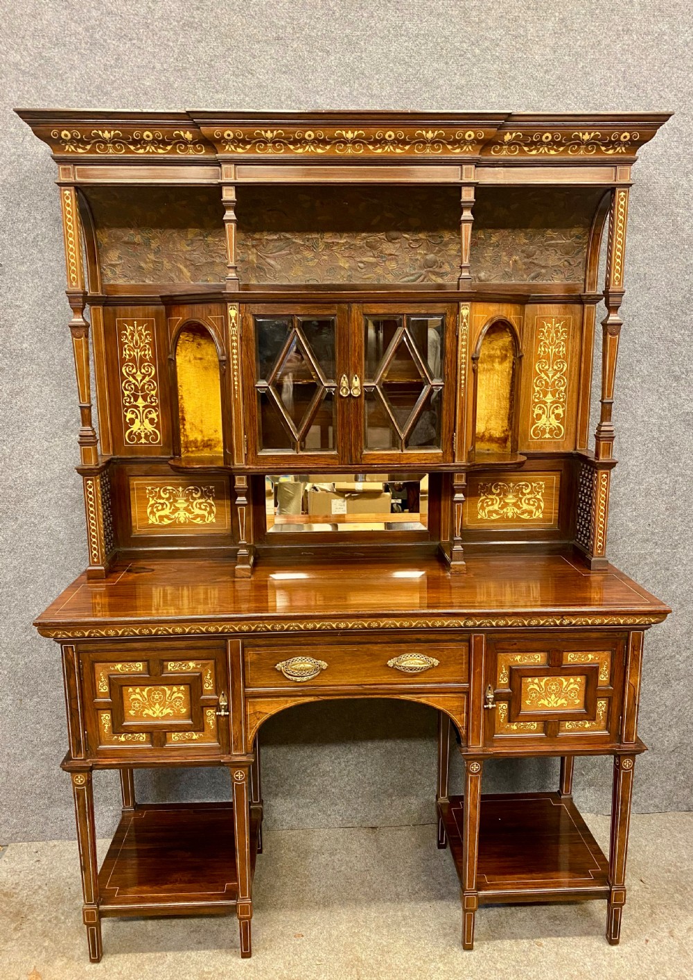 An Aesthetic Movement dark wood side cabinet featuring detailed marquetry inlays, an elevated superstructure with a central glazed cabinet, open niches, a mirror, a single drawer, and lower shelf spaces. View XX