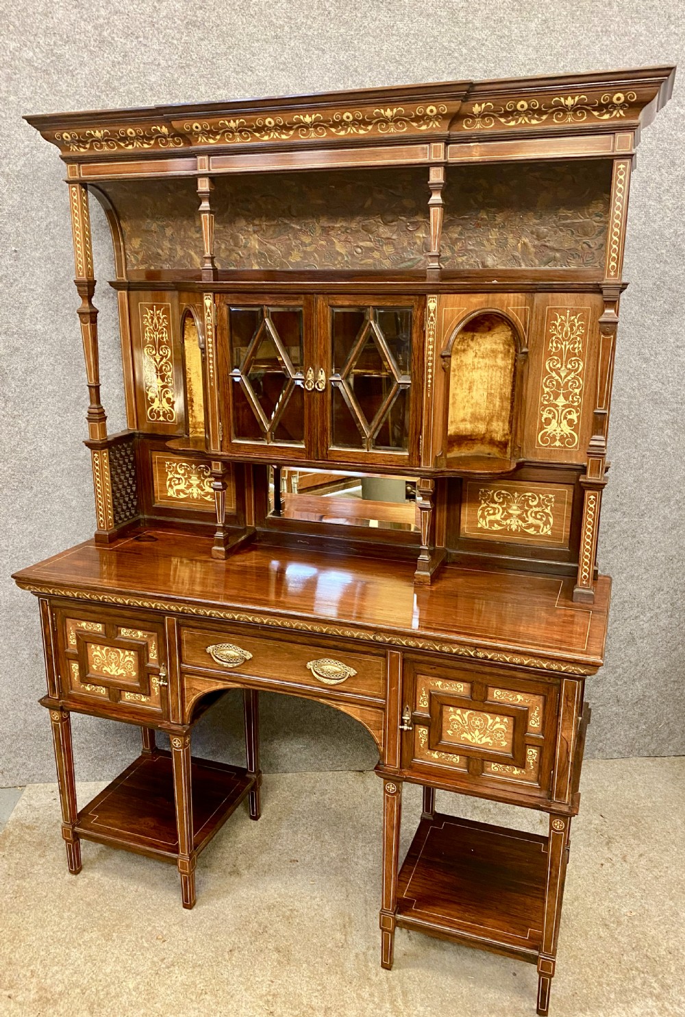 An Aesthetic Movement dark wood side cabinet featuring detailed marquetry inlays, an elevated superstructure with a central glazed cabinet, open niches, a mirror, a single drawer, and lower shelf spaces. View XIV