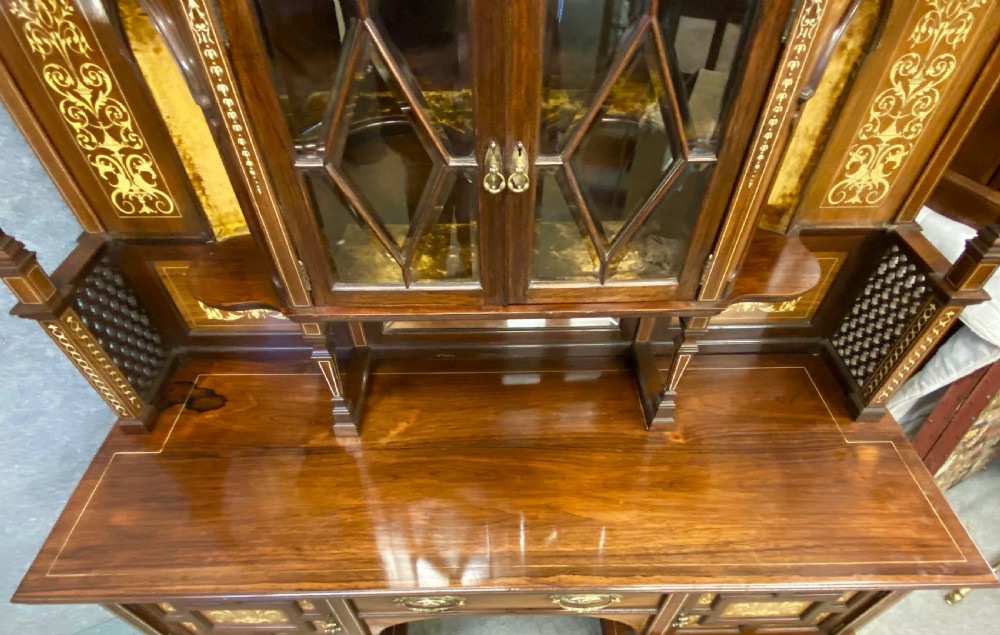 An Aesthetic Movement dark wood side cabinet featuring detailed marquetry inlays, an elevated superstructure with a central glazed cabinet, open niches, a mirror, a single drawer, and lower shelf spaces. View XVII