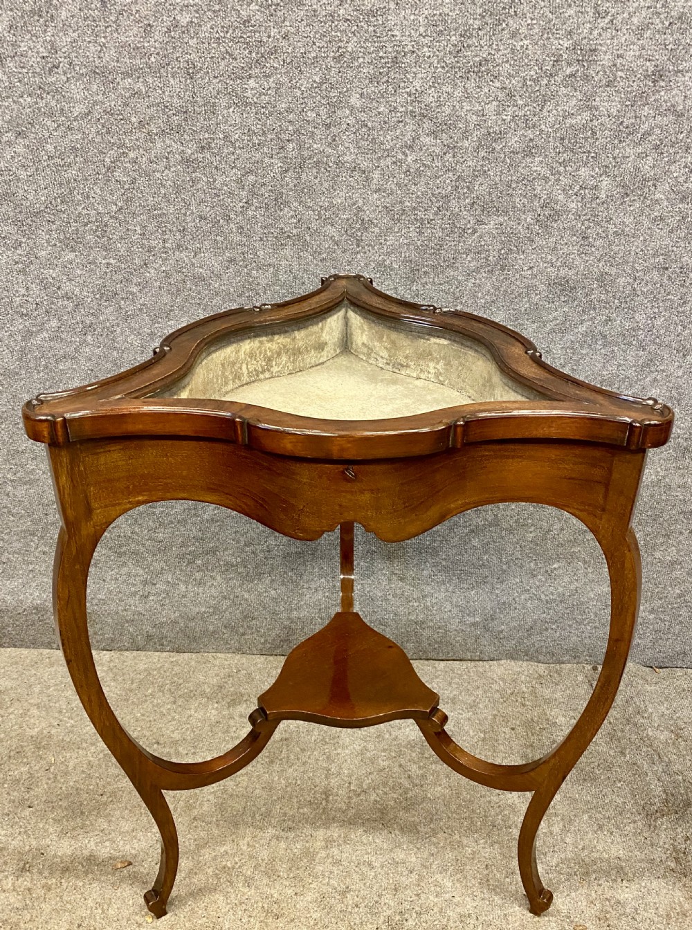 A three-sided serpentine bijouterie table crafted from polished warm brown wood featuring a glass display lid and cabriole legs.