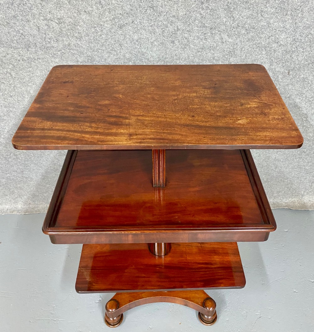 A three-tiered mahogany metamorphic dumb waiter table featuring fluted supports and a shaped quadform base.