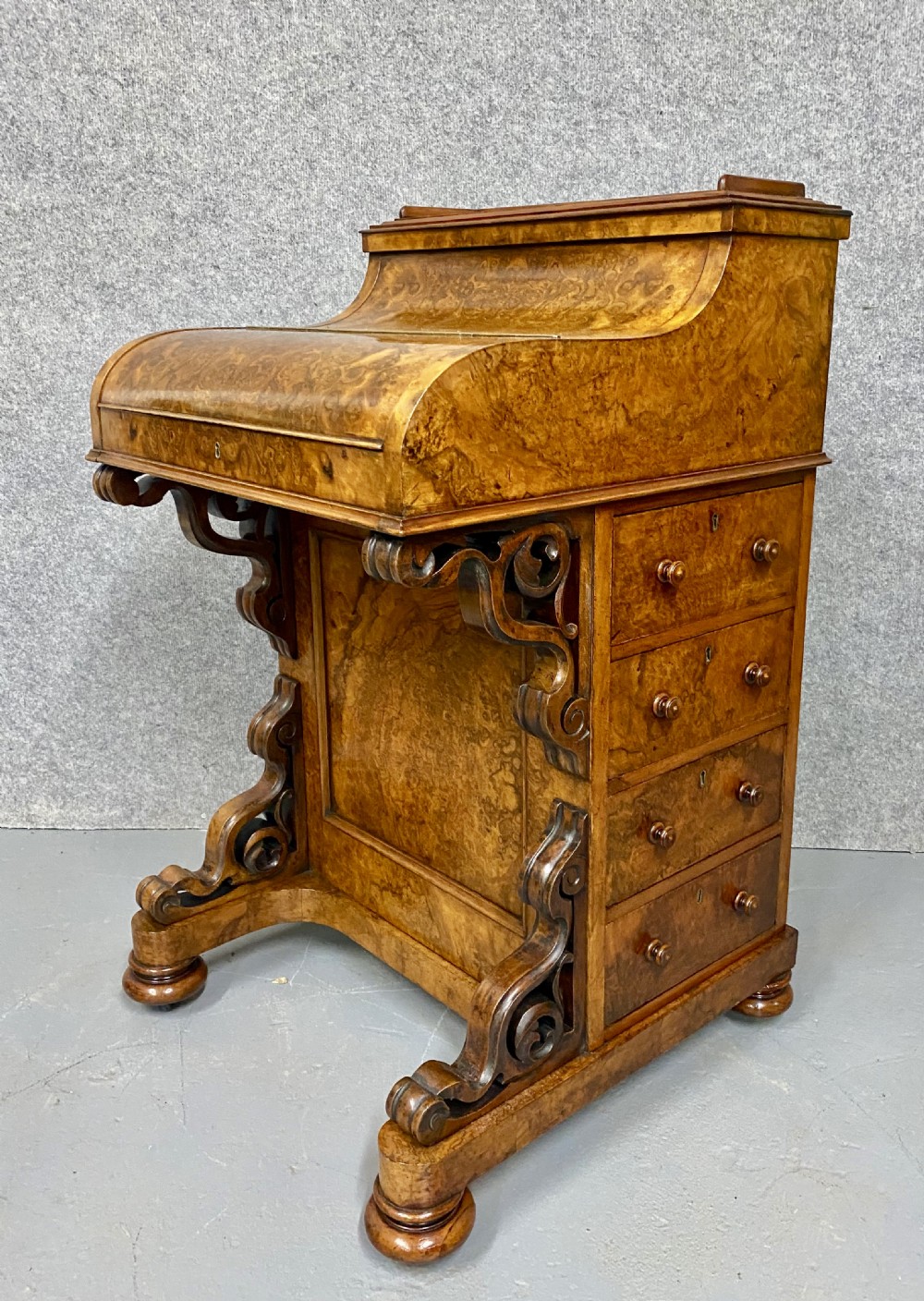 A Victorian burr walnut pop-up davenport desk featuring carved scroll supports, side drawers with wooden knobs, and a curved writing slope.