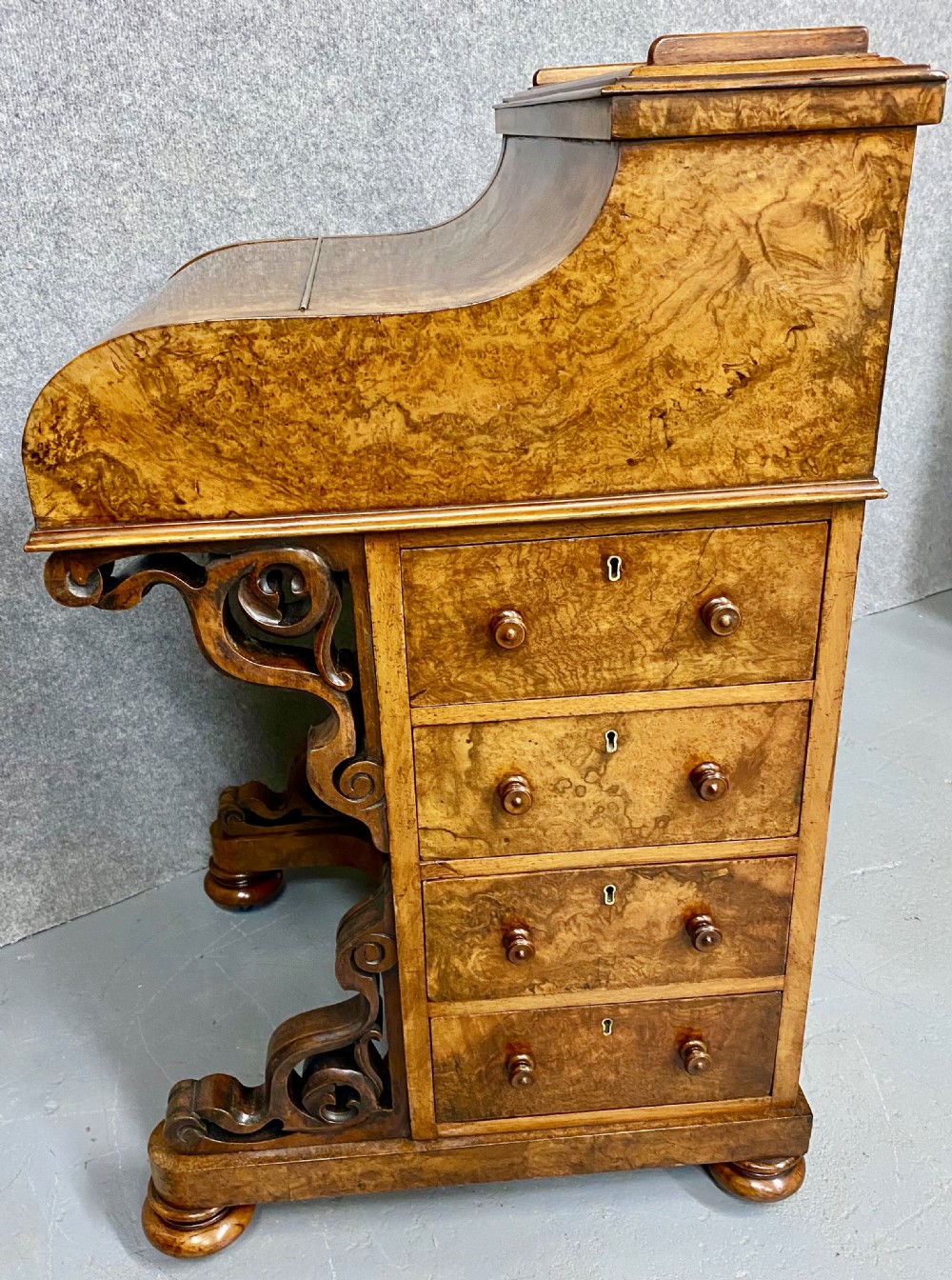 A Victorian burr walnut pop-up davenport desk featuring carved scroll supports, side drawers with wooden knobs, and a curved writing slope. View IX