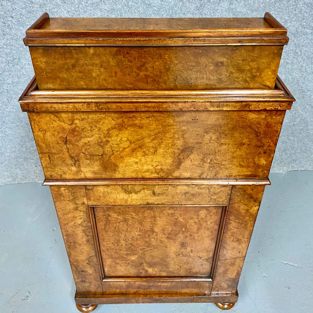 A Victorian burr walnut pop-up davenport desk featuring carved scroll supports, side drawers with wooden knobs, and a curved writing slope. View X