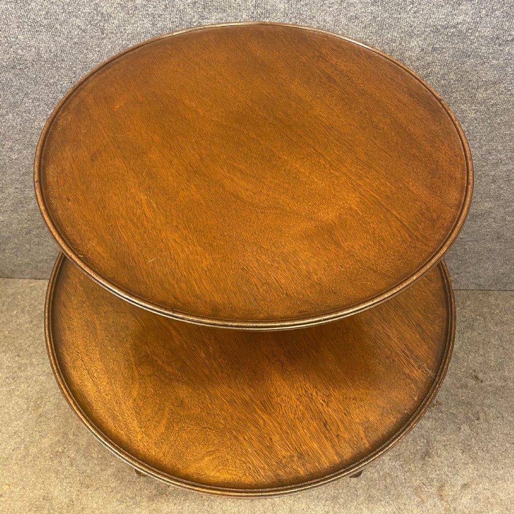 An antique mahogany two-tier occasional table with moulded tray rims, a turned central stem, and a carved tripod base. View II