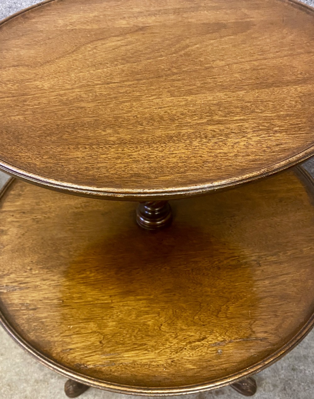 An antique mahogany two-tier occasional table with moulded tray rims, a turned central stem, and a carved tripod base. View VI