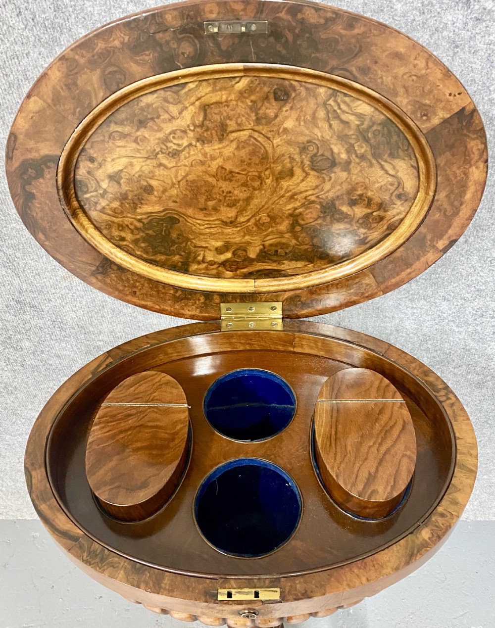 An antique Victorian burr walnut tea poy featuring gadrooned detail around the basin, a fluted central pedestal column, and carved scroll feet on castors. View V
