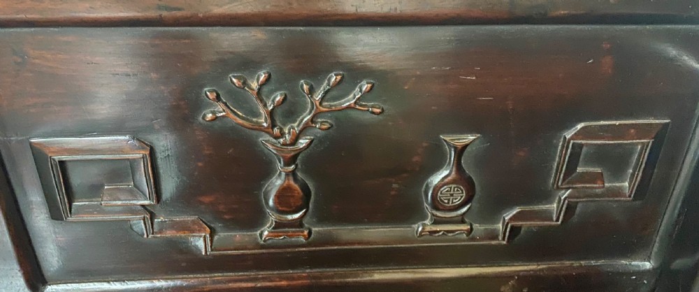 A dark hardwood Chinese bench featuring relief carved back panels depicting scholars objects, low side armrests, and an intricate apron with key fret motifs. View V
