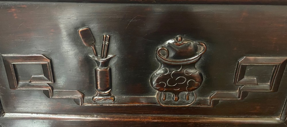 A dark hardwood Chinese bench featuring relief carved back panels depicting scholars objects, low side armrests, and an intricate apron with key fret motifs. View VI