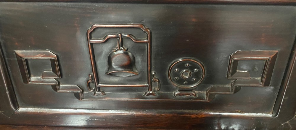 A dark hardwood Chinese bench featuring relief carved back panels depicting scholars objects, low side armrests, and an intricate apron with key fret motifs. View VII