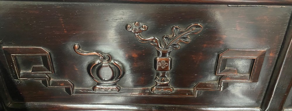 A dark hardwood Chinese bench featuring relief carved back panels depicting scholars objects, low side armrests, and an intricate apron with key fret motifs. View IX