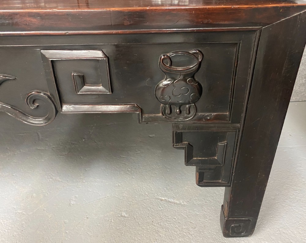 A dark hardwood Chinese bench featuring relief carved back panels depicting scholars objects, low side armrests, and an intricate apron with key fret motifs. View X