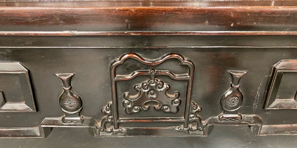 A dark hardwood Chinese bench featuring relief carved back panels depicting scholars objects, low side armrests, and an intricate apron with key fret motifs. View XI