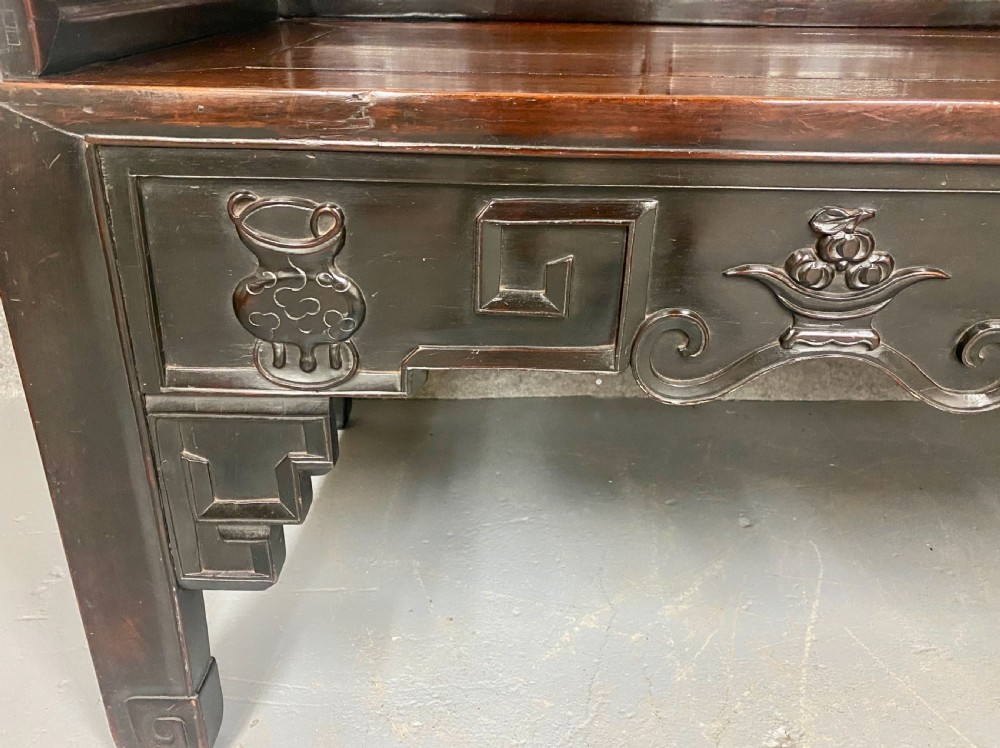 A dark hardwood Chinese bench featuring relief carved back panels depicting scholars objects, low side armrests, and an intricate apron with key fret motifs. View XIII