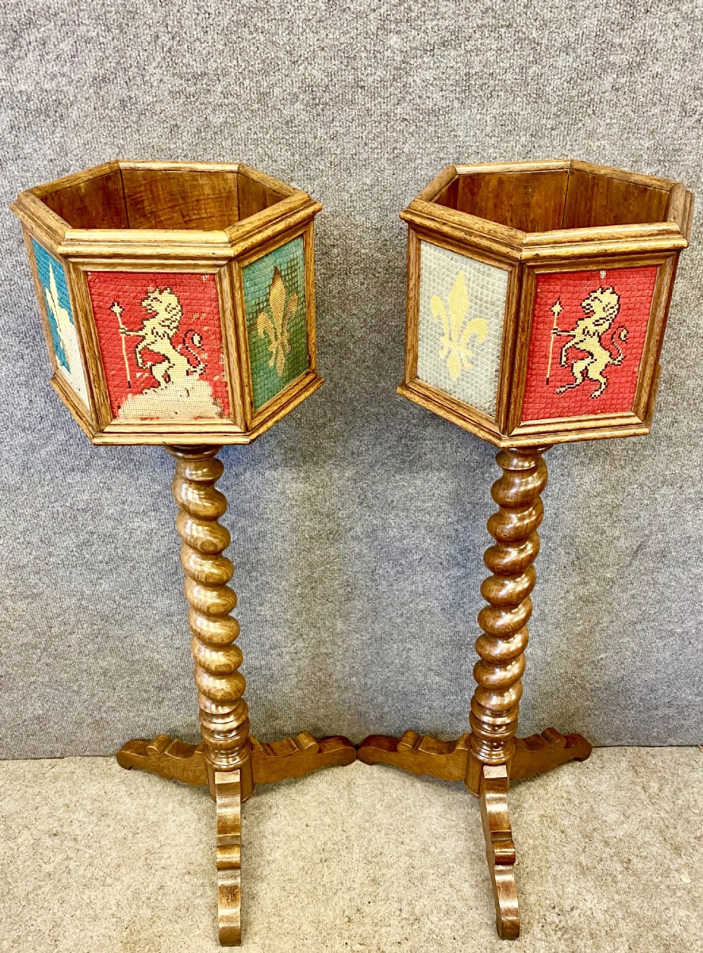 A pair of oak medieval style plant stands featuring hexagonal needlepoint tops decorated with fleur-de-lis and lion heraldic motifs on barley twist stems with tripod bases. View III