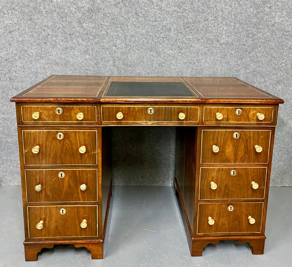 A Regency mahogany pedestal partners desk featuring a central green leather inset writing surface, brass knob handles, and stringing inlay.