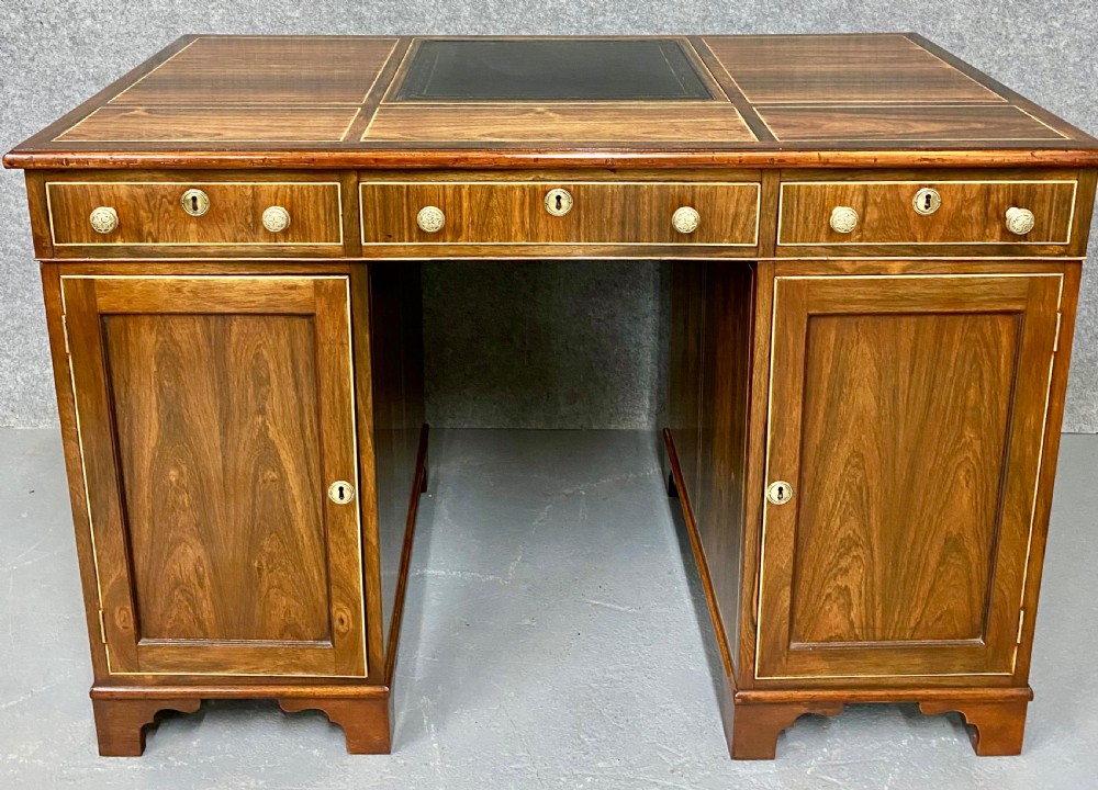 A Regency mahogany pedestal partners desk featuring a central green leather inset writing surface, brass knob handles, and stringing inlay. View IV