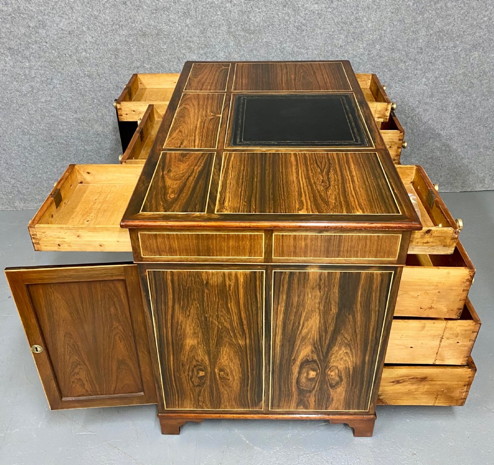 A Regency mahogany pedestal partners desk featuring a central green leather inset writing surface, brass knob handles, and stringing inlay. View VII