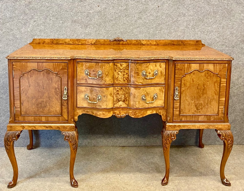 A nine-piece Queen Anne style dining room suite featuring a burr walnut dining table, matching sideboards, and red patterned fabric chairs with cabriole legs. View IV