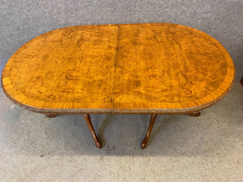 A nine-piece Queen Anne style dining room suite featuring a burr walnut dining table, matching sideboards, and red patterned fabric chairs with cabriole legs. View VII