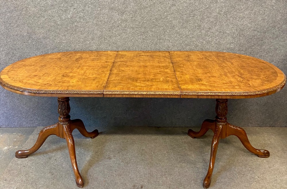 A nine-piece Queen Anne style dining room suite featuring a burr walnut dining table, matching sideboards, and red patterned fabric chairs with cabriole legs. View VIII