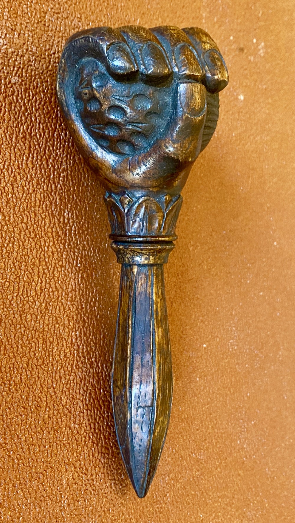 An antique hand-carved wooden treen nutcracker shaped as a human fist clasping a textured ball, resting atop a faceted handle.