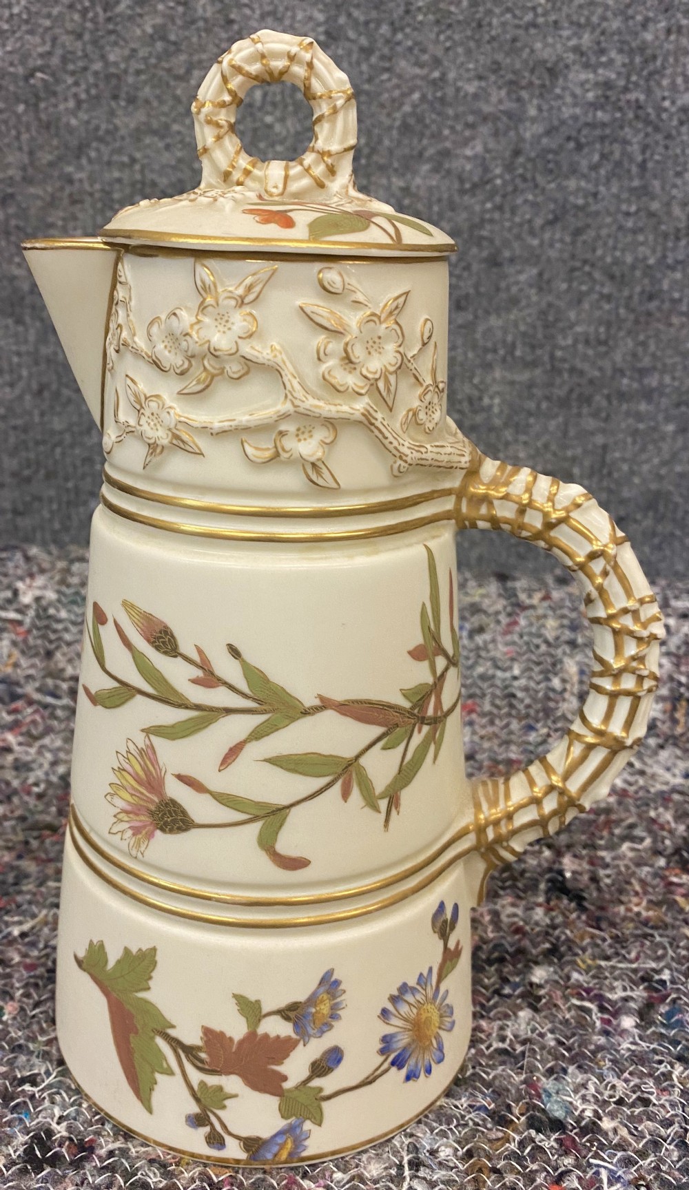 An antique ivory porcelain coffee pot featuring hand-painted floral motifs, relief blossom moulding, and a gilded lattice handle and finial.