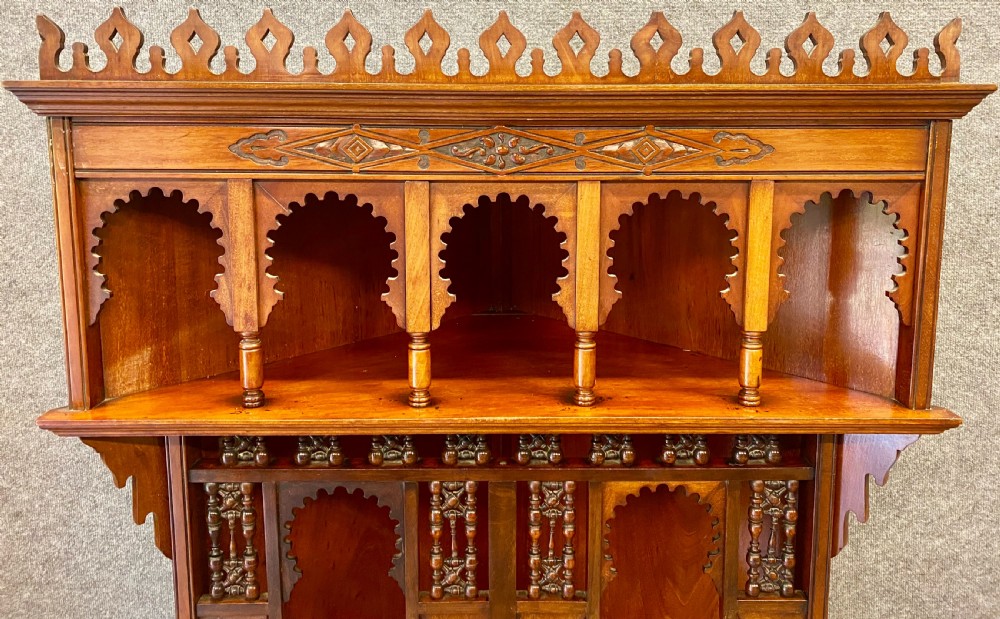 A late nineteenth-century Anglo-Moorish tiered wooden corner cabinet featuring mashrabiya fretwork, horseshoe arches, starburst door panels, and two drawers with brass pulls. View V